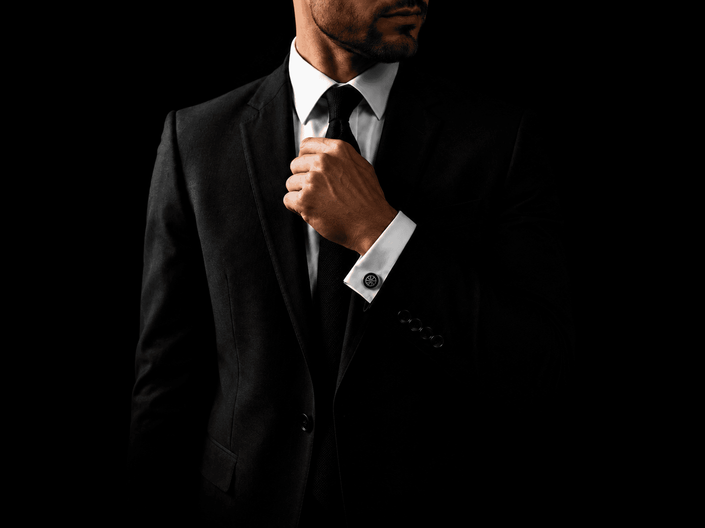Luxury black suit with premium Cufflinkk cufflinks on a white shirt cuff against a minimalist black background.
